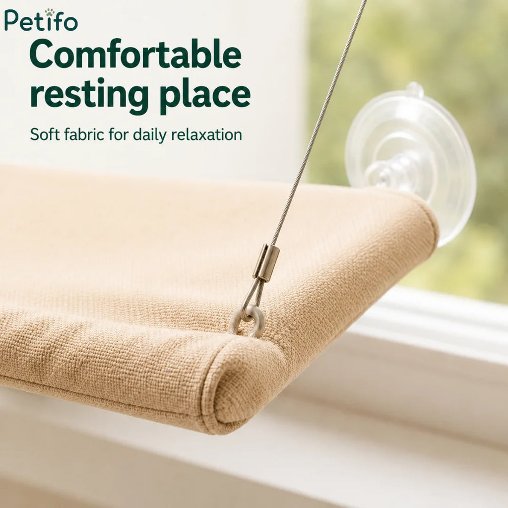 A close-up view of the beige soft fabric and stainless steel hanging cable of the cat hammock next to a clear suction cup.