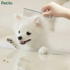 A person using a Petifo stainless steel grooming comb on a small, fluffy white dog against a light background.