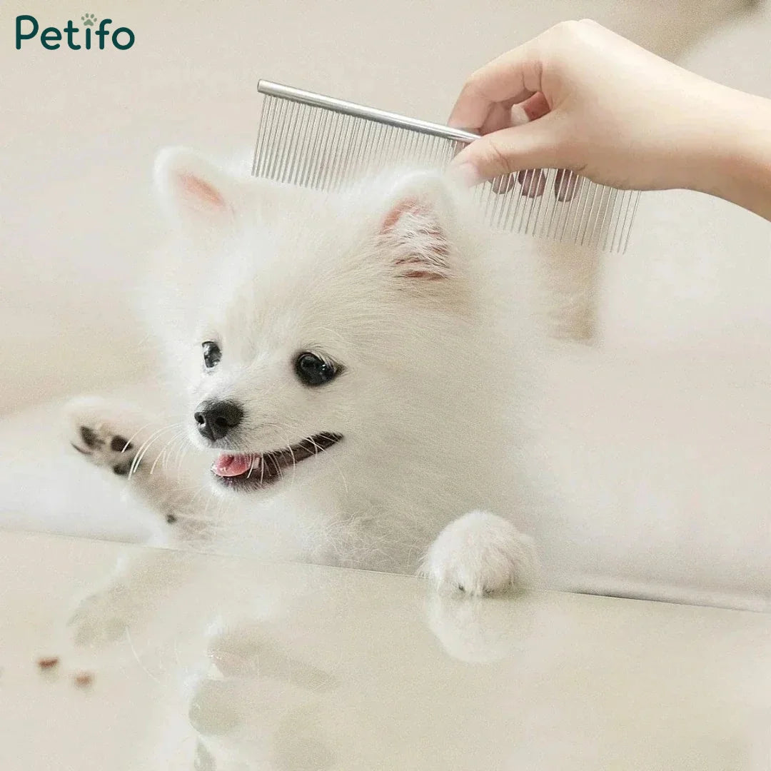 A person using a Petifo stainless steel grooming comb on a small, fluffy white dog against a light background.