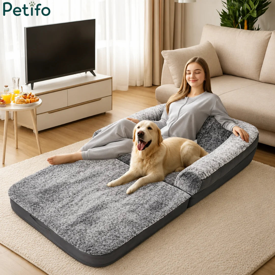 A relaxed woman lounging on a versatile, plush grey pet sofa bed next to her happy golden retriever in a modern living room.