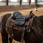 Close-up view of a black padded western saddle cushion installed on a brown horse in an indoor riding arena.