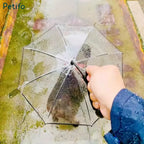 A person holding a clear umbrella outdoors in the rain with a wet pathway visible beneath.