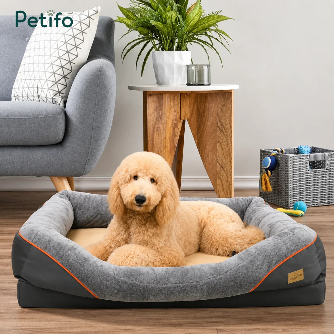 A fluffy, light-colored dog resting comfortably in a soft-bolstered orthopedic pet bed placed in a modern living room setting.