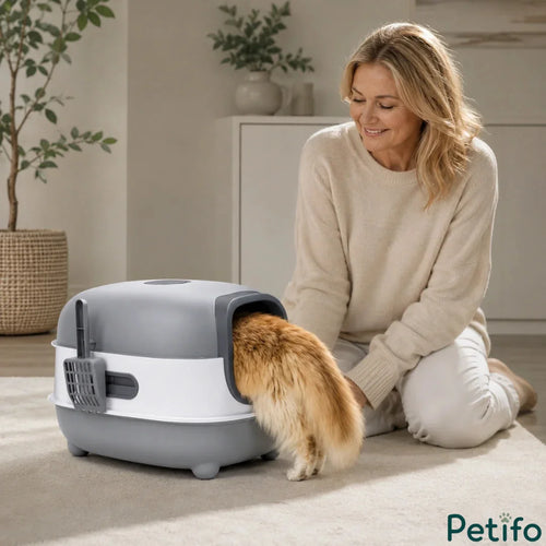 Woman smiling while looking at her cat entering a covered grey and white cat litter box in a bright living room.