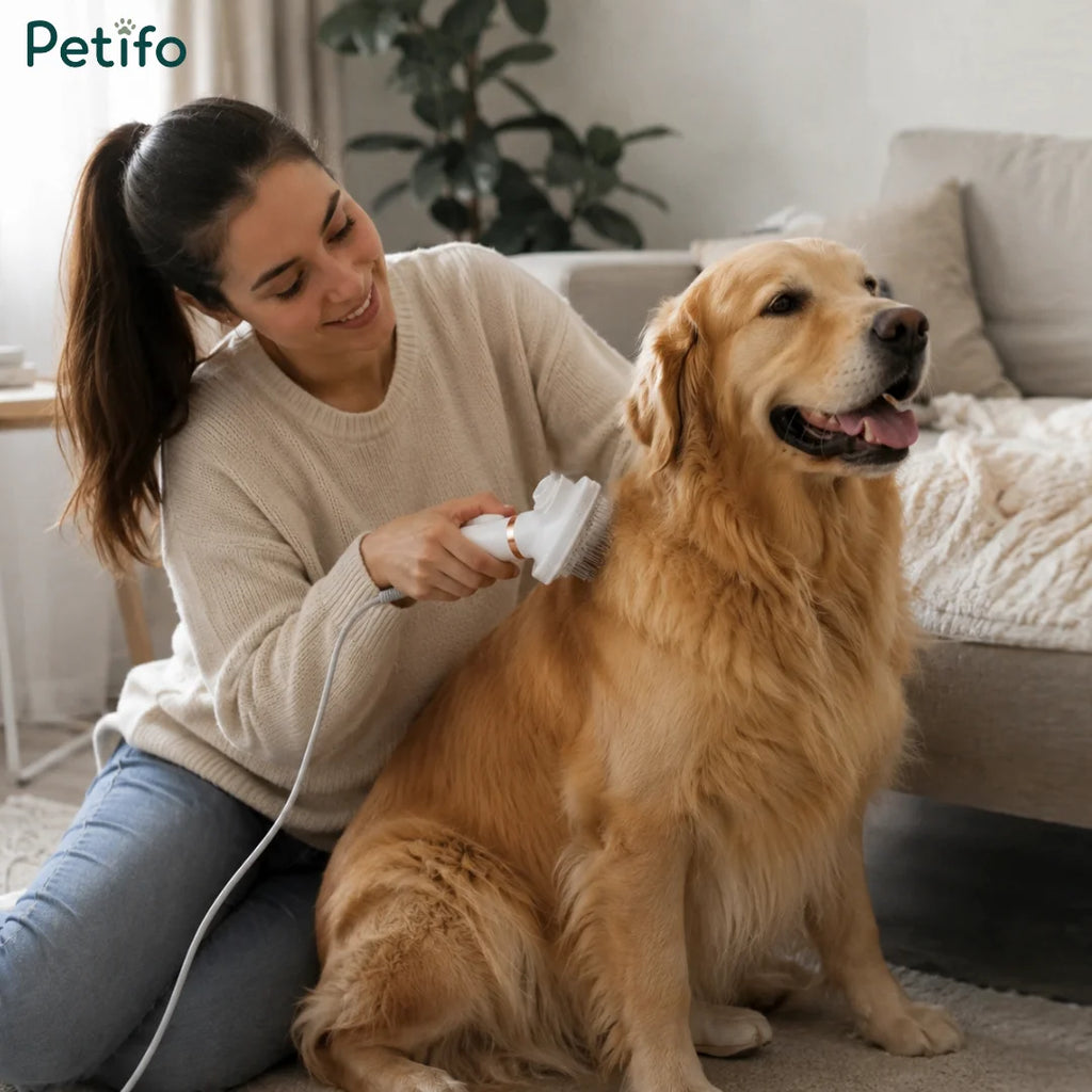 Woman sitting on the living room floor gently brushing a happy golden retriever with a white electric grooming brush.