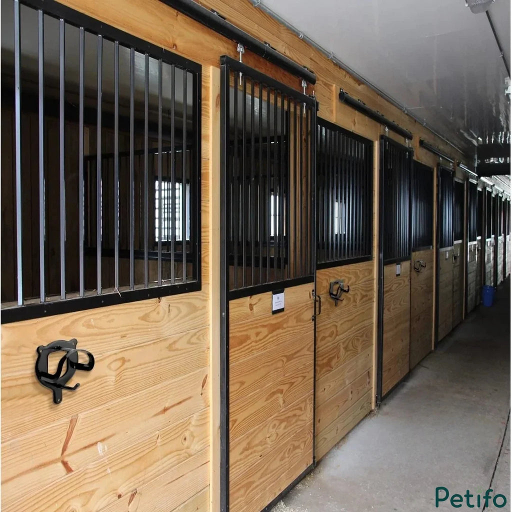 Black wall-mounted bridle rack installed on wooden stable doors in a professional equestrian barn.