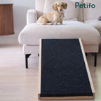 A small dog sitting on a sofa next to an adjustable wooden pet ramp featuring a non-slip texture for safe climbing.