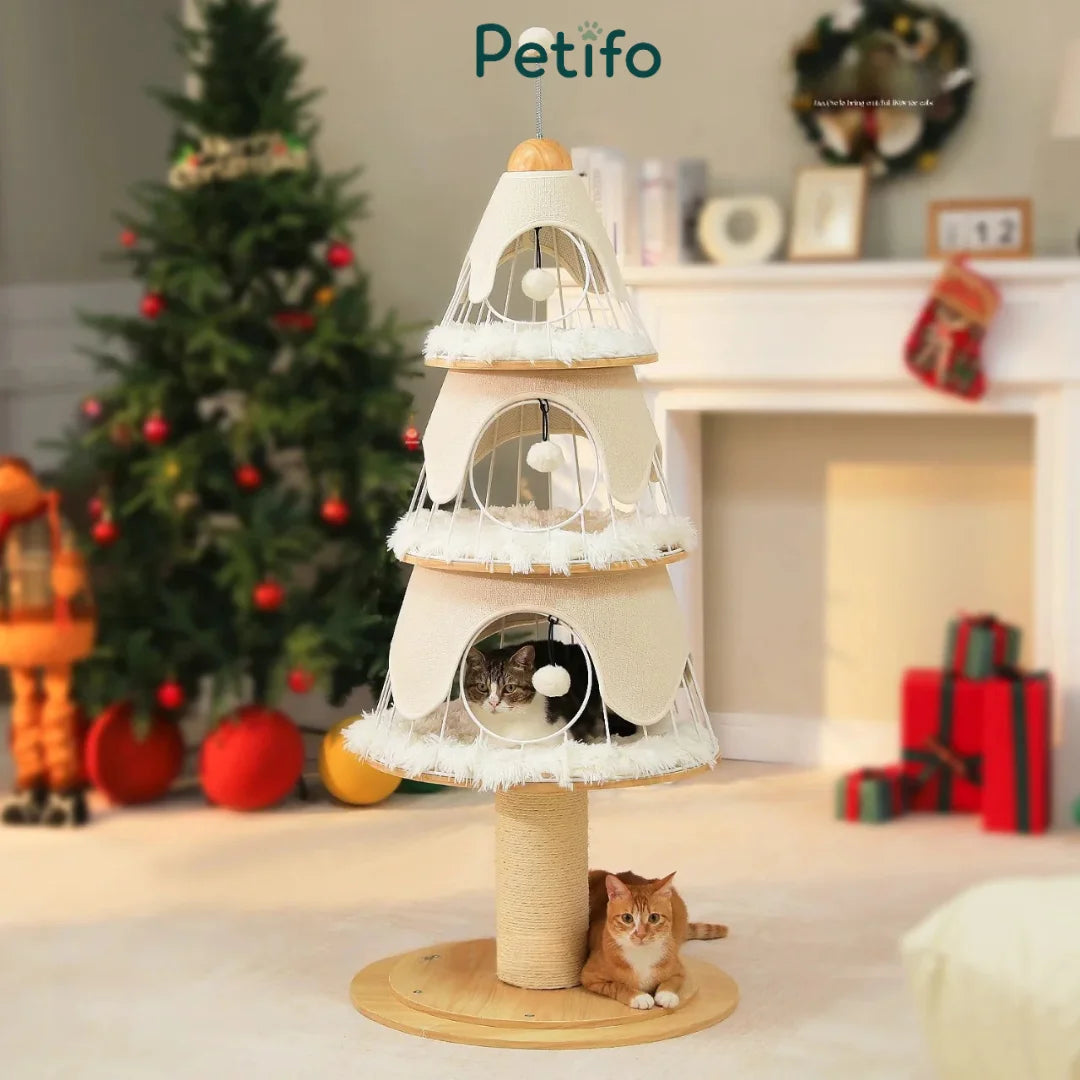 A three-tier, cream-colored, Christmas tree-themed cat tower featuring cozy perches and a hanging toy, displayed in a festive holiday living room.