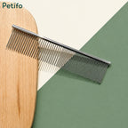 Flatlay product shot of the Petifo metal pet grooming comb resting against a wooden board and a green and cream background.