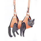 A gray cat secured inside an orange Petifo grooming hammock hanging against a white background.