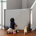 Child riding a toy bike and dog looking toward a grey retractable mesh safety gate at the bottom of stairs.