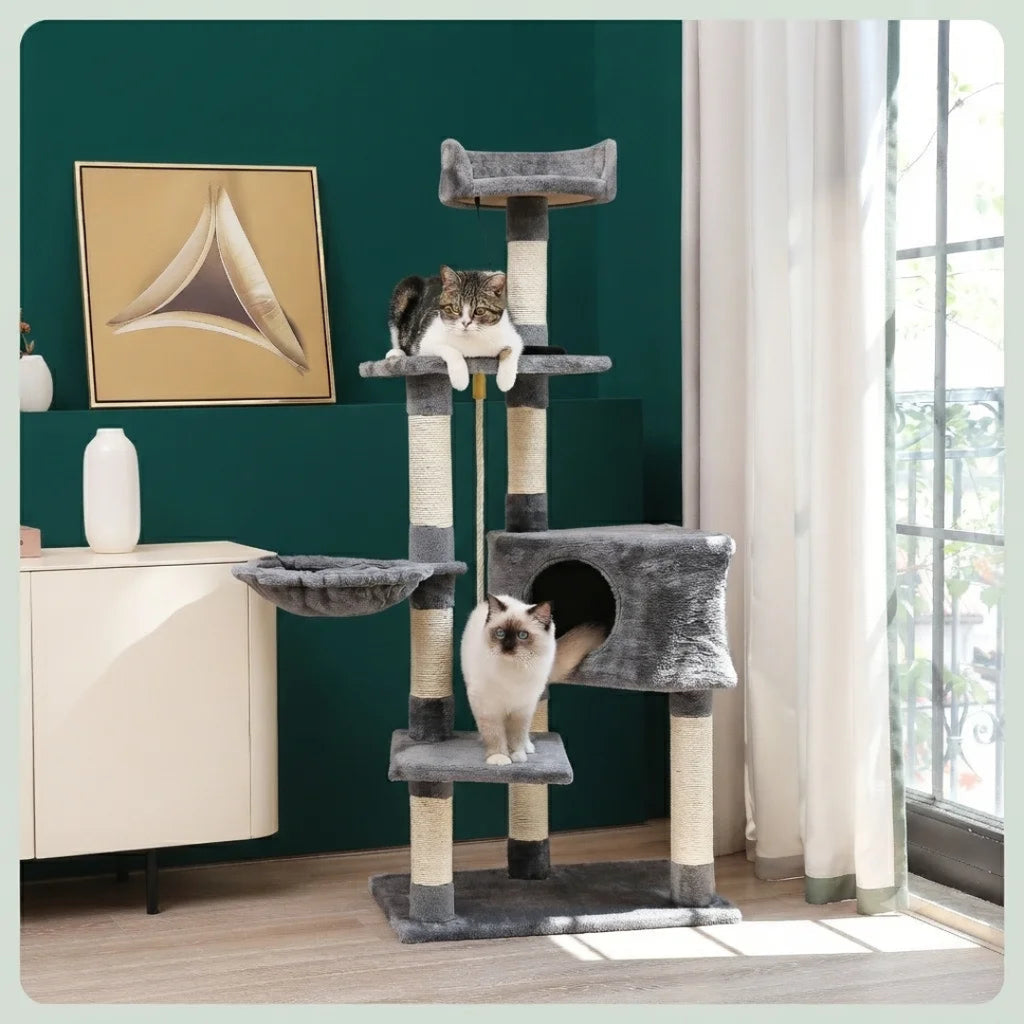 Three cats playing on a grey multi-level cat tree positioned in a bright room, showcasing a hanging hammock, a central condo, and a top viewing platform.