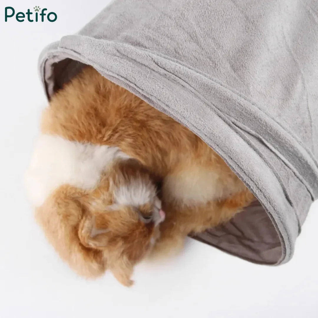 Fluffy orange and white cat curled up sleeping soundly inside a grey plush cat tunnel.