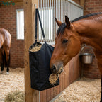A brown horse eating hay from a black hanging slow feeder bag inside a stable stall.