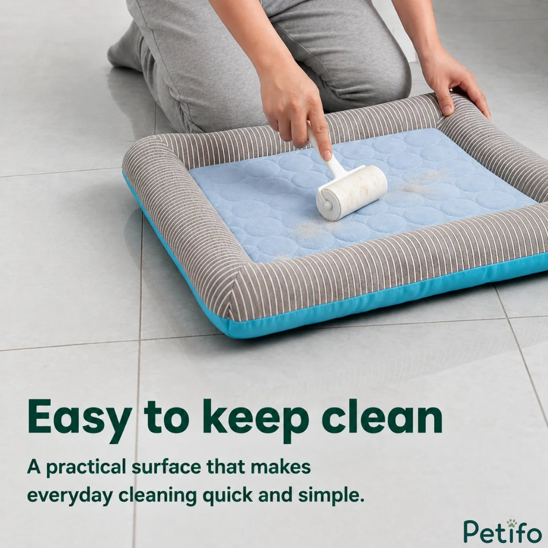 A person using a lint roller to clean pet hair off the surface of a blue and grey striped cooling pet bed.