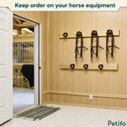 Organized equestrian tack room featuring wooden walls fitted with black metal bridle and halter hooks.