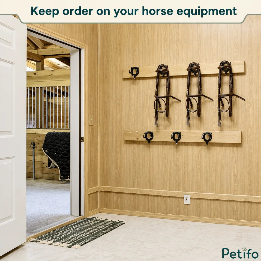 Organized equestrian tack room featuring wooden walls fitted with black metal bridle and halter hooks.