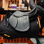  Black English saddle resting on a black quilted saddle pad on a wooden rack.
