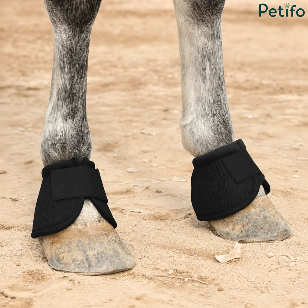 Horse wearing black protective hoof boots on sandy ground
