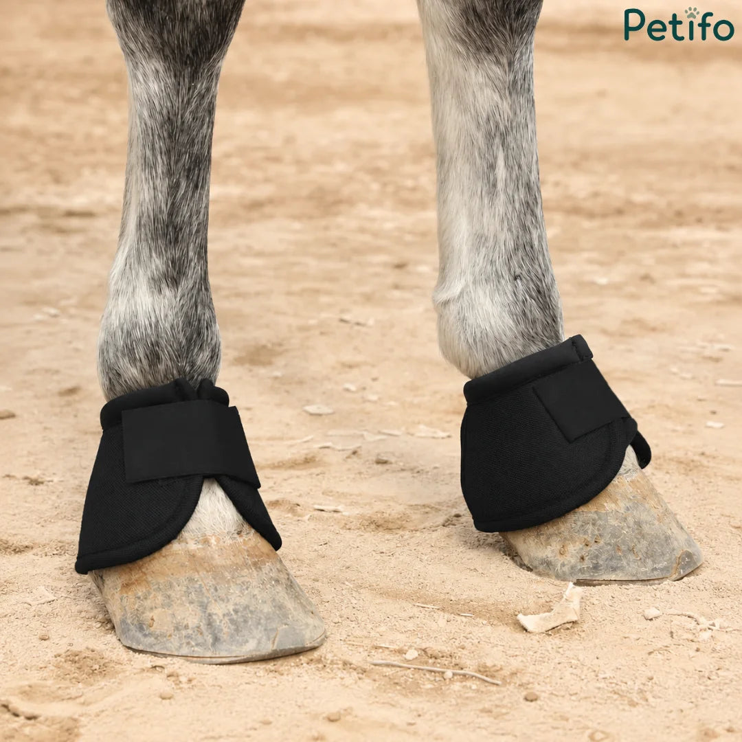 Horse wearing black protective hoof boots on sandy ground