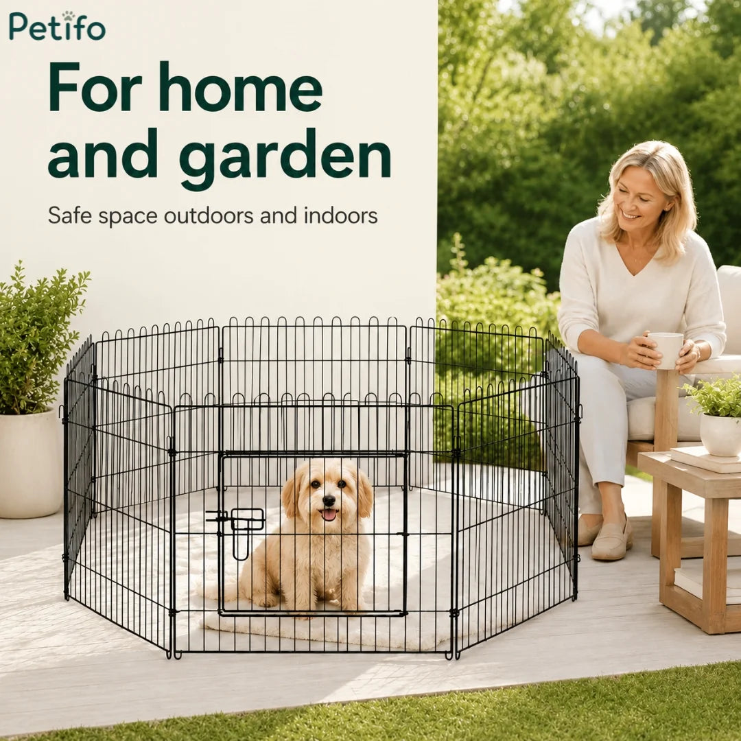 Puppy inside the wire playpen set up on a home patio next to a sitting woman.