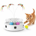 An energetic orange kitten playing with a white 3-in-1 interactive cat toy featuring spinning butterflies and colorful rolling balls.
