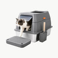 A cat exiting a modern, covered stainless steel litter box with a grey hood, door, and matching litter-trapping mat.
