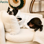 A Boston Terrier in a bathrobe relaxing on a luxury white plush pet sofa in a decorated living room.