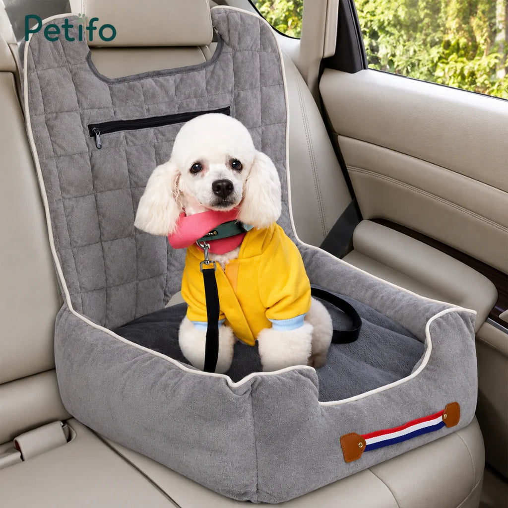 A white poodle sitting comfortably in a soft, grey Petifo dog car seat secured on a vehicle's back seat.