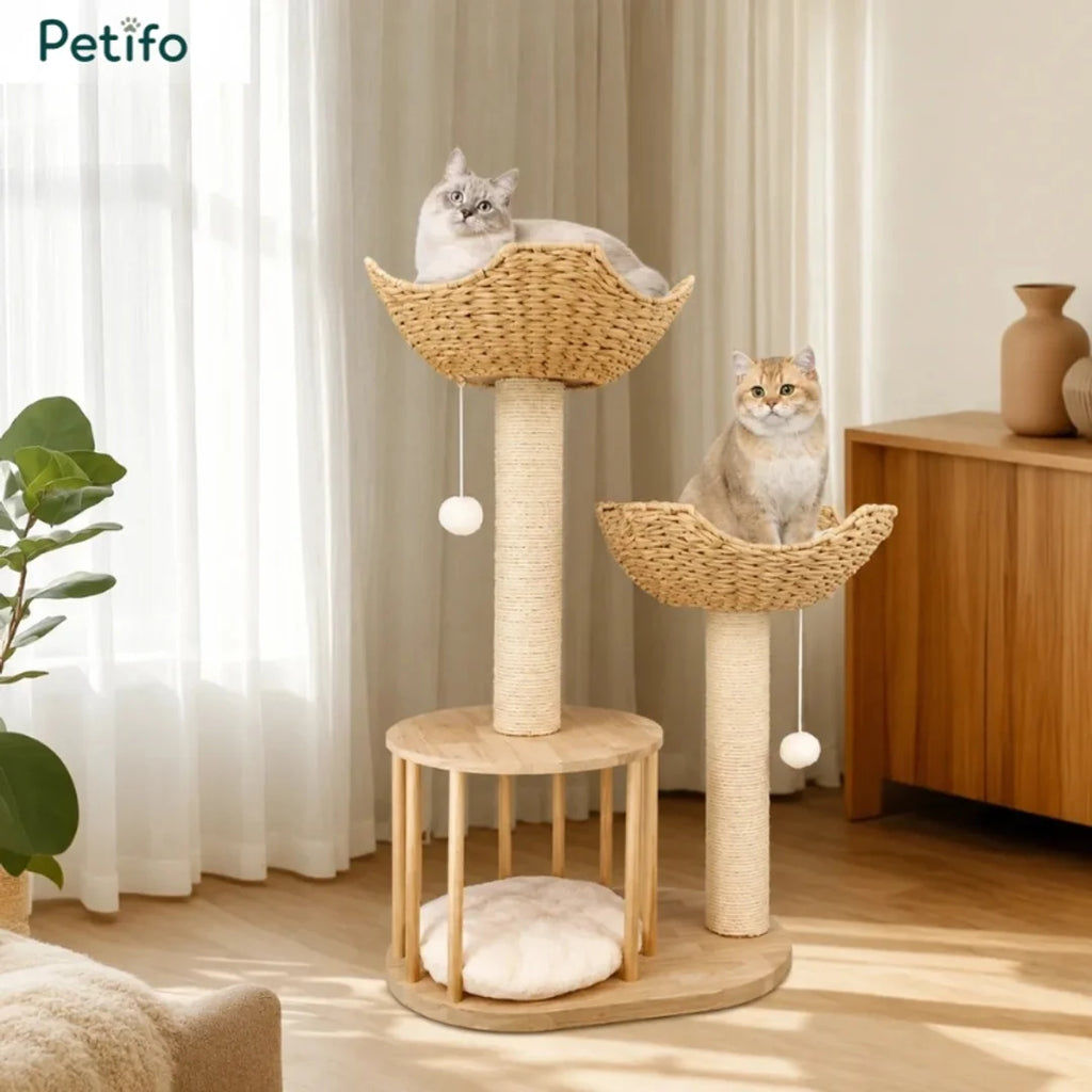 Two cats sitting inside the handwoven wicker baskets of a Petifo wooden cat tree in a cozy home interior.