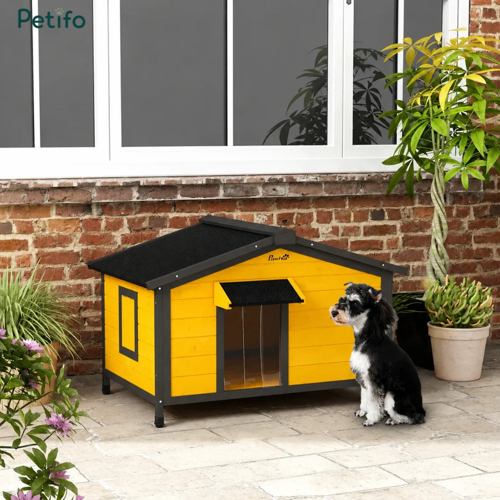 A small dog sitting next to a stylish yellow and black outdoor wooden dog house on a patio.