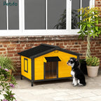 A small dog sitting next to a stylish yellow and black outdoor wooden dog house on a patio.
