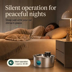 A peaceful bedroom scene showing a woman sleeping and a cat resting on a bed next to a silent-operation, 30 dB stainless steel pet water fountain.